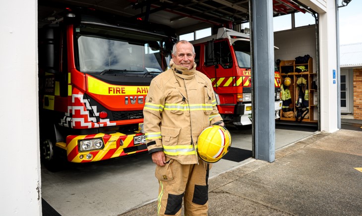 Fire officer Shane Bromley wearing his uniform in front of two fire engines.